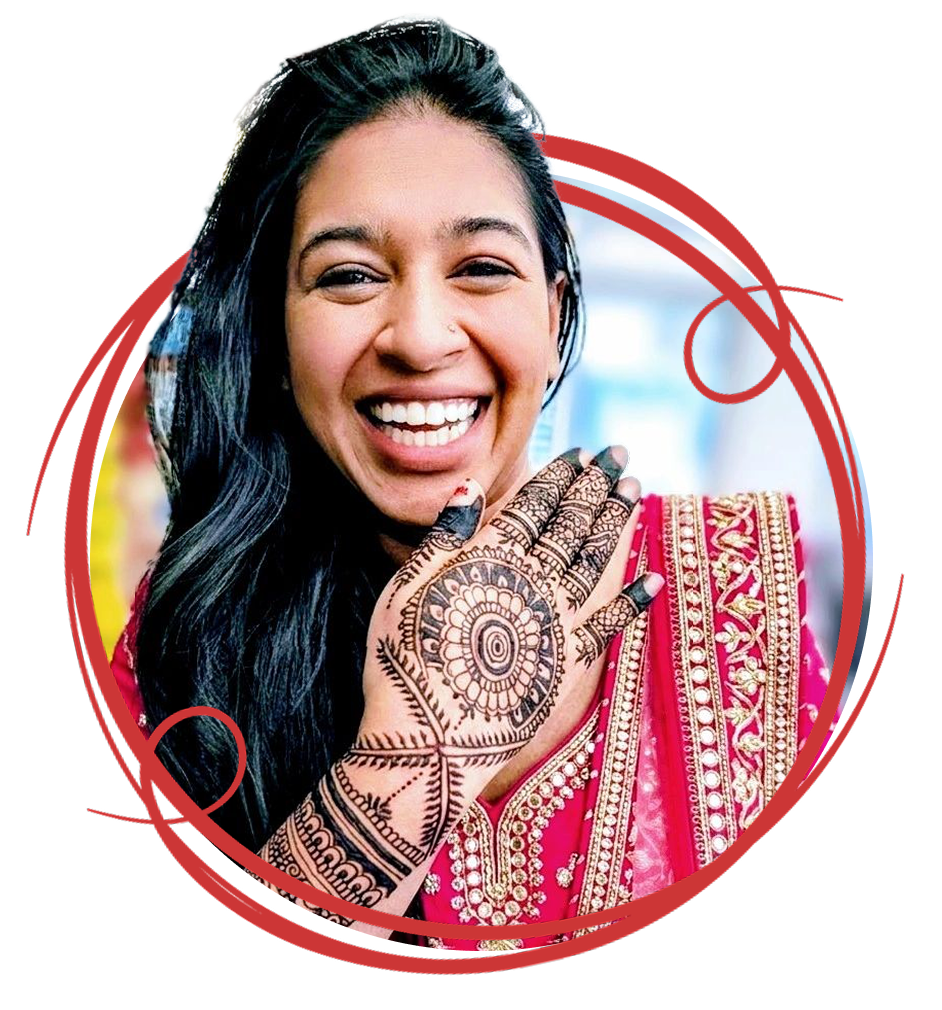 Headshot of Rufsana Begum, showing face and torso, wearing a pink sari, she's raised her hand up to show intricate henna decorations